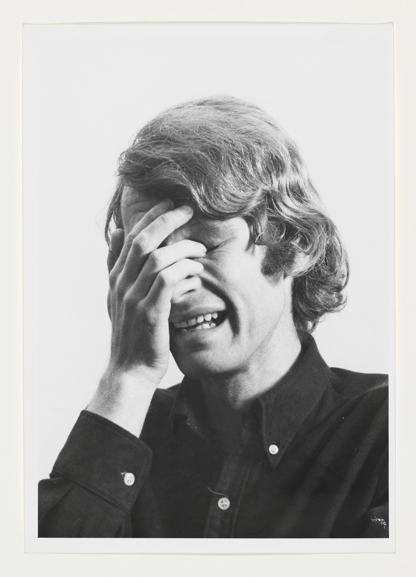 Black and white photo of a person with medium-length hair, covering their face with one hand, appearing to cry.